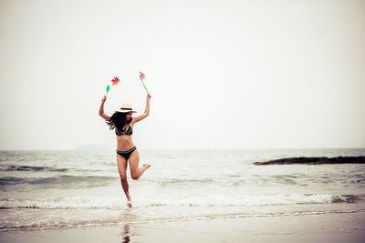 Full length of woman holding pinwheel toys while running at beach