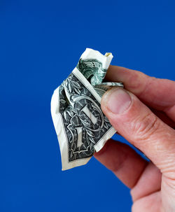 Cropped hand holding crumpled paper currency against blue background