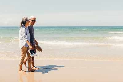 Romantic senior couple strolling happily along the beach in the sunshine and bright sky. 