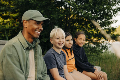 Kids sitting with smiling counselor wearing cap at summer camp