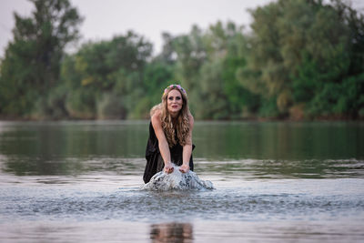 Portrait of young woman in lake against trees