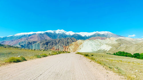 Road leading towards mountains against clear blue sky