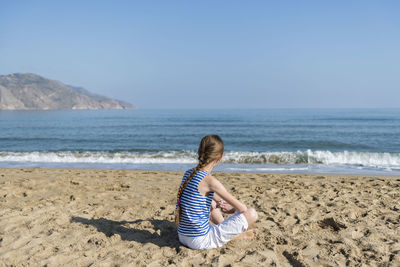 Rear view of girl sitting on beach against sky