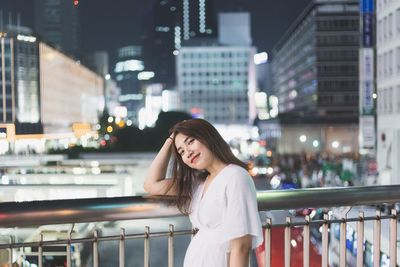 Portrait of young woman standing against railing in city