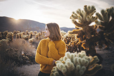 A woman is standing near a cactus in the desert of california