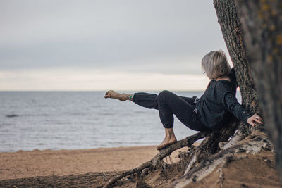 Young woman relaxing on sand at beach against sky