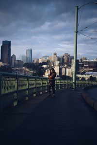Full length portrait of man standing on railing in city