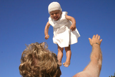 Low angle view of father throwing baby girl against clear sky