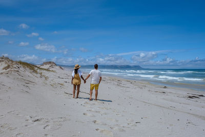 Rear view of woman walking at beach against sky