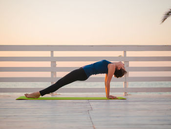 Full length of woman doing yoga on promenade against clear sky during sunrise