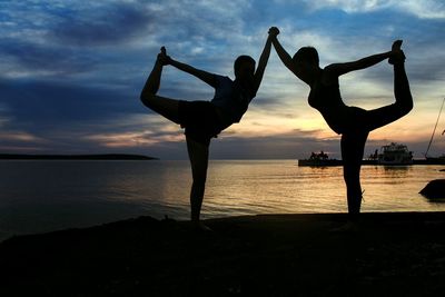 Silhouette women doing yoga at beach during sunset