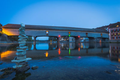 Illuminated bridge over river against clear sky at dusk