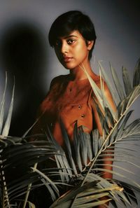 Portrait of young woman by plants standing against wall