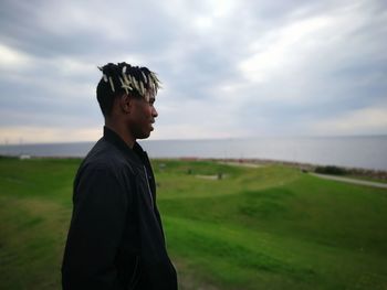 Side view of man standing on field against sky