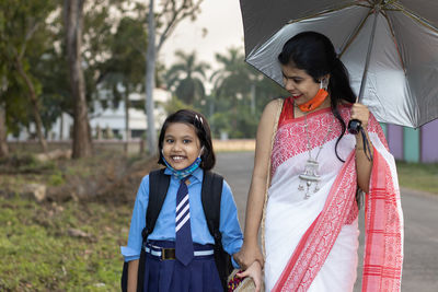 An indian school girl child going to school again after pandemic with her mother wearing nose mask 