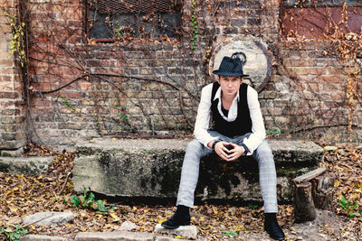 Portrait of vintage styled man with fedora hat sitting outdoors and looking at camera.