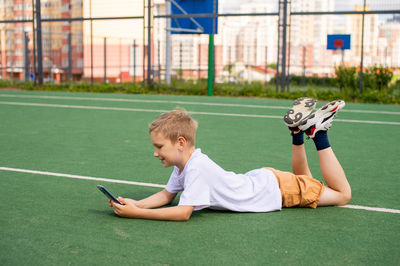 The boy is lying on the floor and playing with the phone