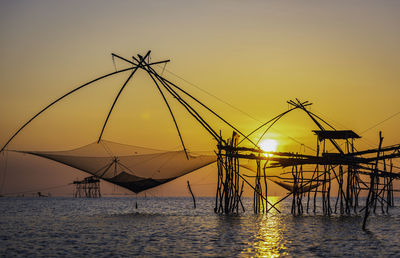 Silhouette fishing net by sea against sky during sunset