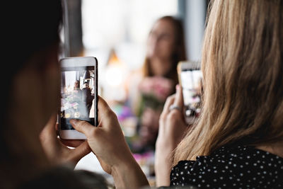 Women photographing friend through smart phones at dining table in restaurant