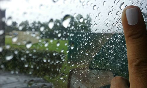 Cropped image of woman touching wet glass window during monsoon