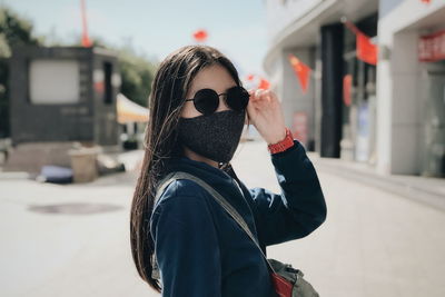 Portrait of woman wearing mask and sunglasses while standing outdoors