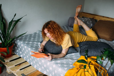 Woman working from home on bed using graphics tablet for design and drawing