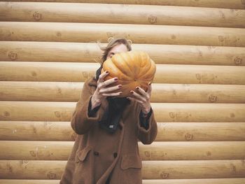 Close-up of woman holding pumpkin against wall