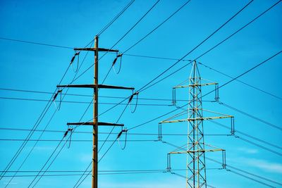 Low angle view of electricity pylon against blue sky