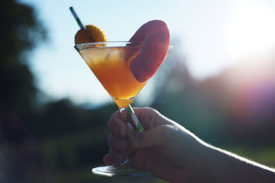 Hand holding orange peach cocktail in glass with ice cubes and straw