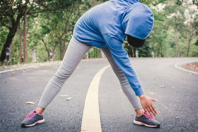 Woman exercising on road amidst trees