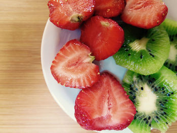 Slices of strawberries and kiwi fruit in plate on table