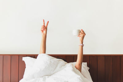 Female hand showing the funny sign and holding coffee cup behind blanket in the bed.