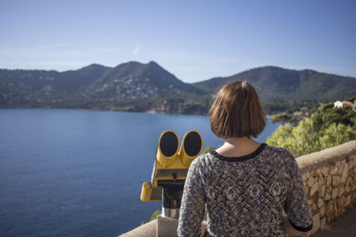 Rear view of woman standing by coin-operated binoculars at observation point against mountain