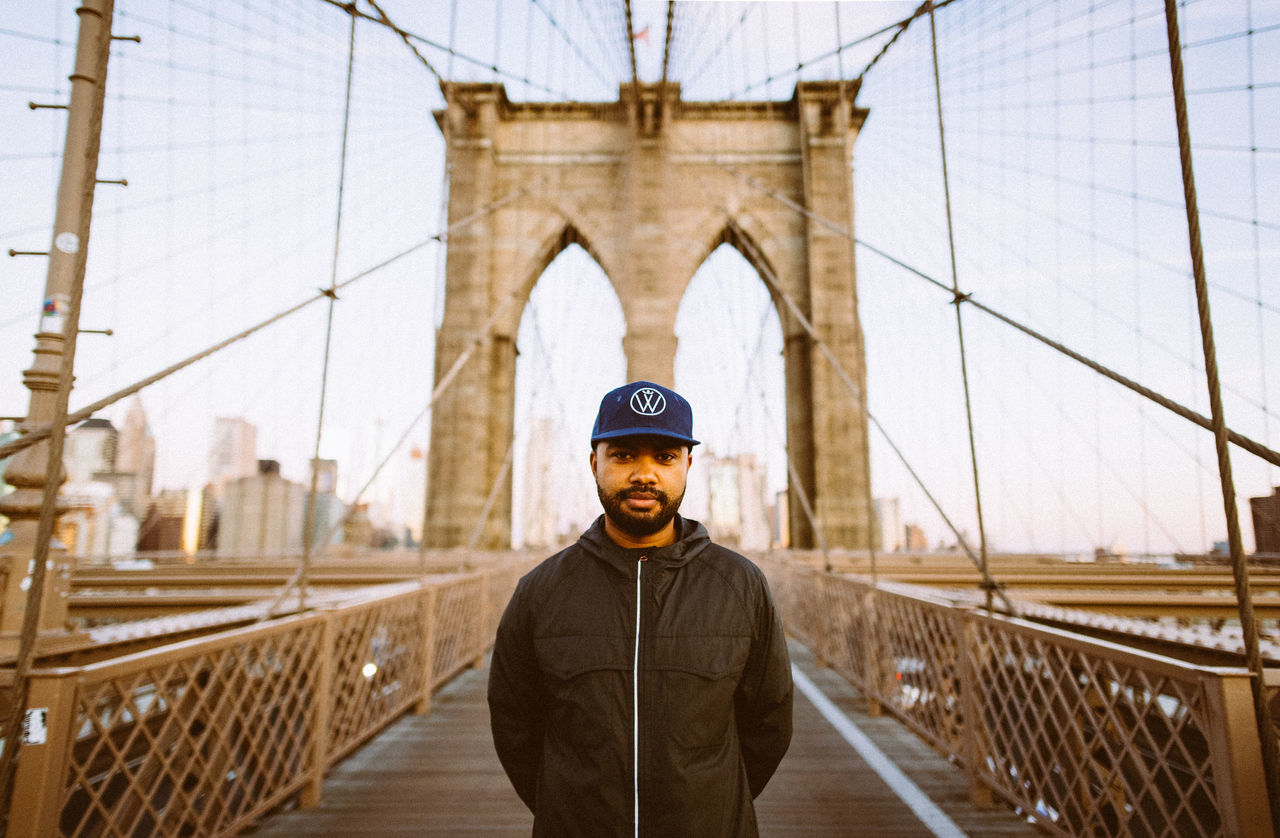 PORTRAIT OF MAN STANDING ON SUSPENSION BRIDGE