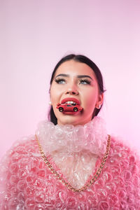 Young woman wearing bubble wrap with toy car in mouth against colored background