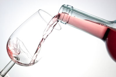 Close-up of wine pouring from bottle in glass against white background