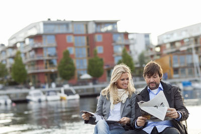 Couple sitting by water and reading newspaper