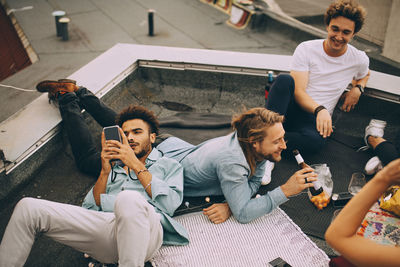 Man texting on mobile phone while friends enjoying beer on terrace at party