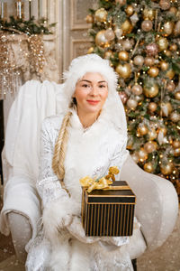 Snow maiden holding. gift while sitting in a chair by the christmas tree