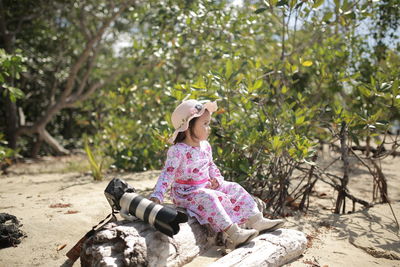 Cute girl sitting on plants against trees