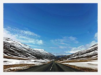 Road amidst snowcapped mountains against blue sky