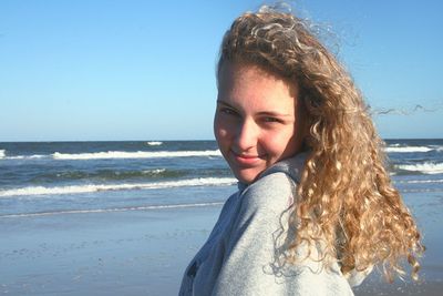 Portrait of smiling young woman standing at beach against clear sky