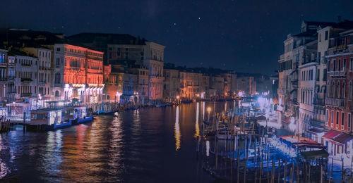 Boats moored at harbor against buildings in city at night