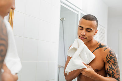 Man wiping face while looking into mirror at bathroom