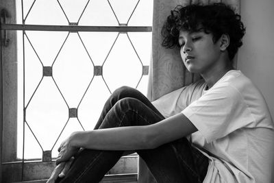 Side view of young man looking away while sitting on window