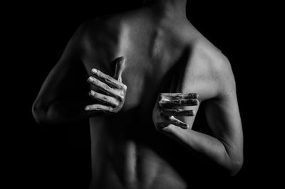 Midsection rear view of shirtless man with hands behind back against black background