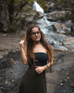Portrait of young woman standing against waterfall