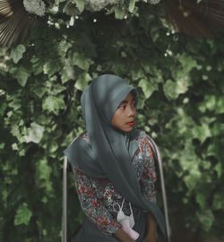 Young woman looking away while standing against trees