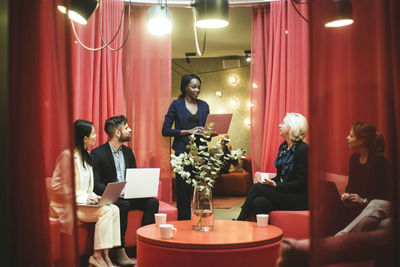 Businesswoman holding laptop while discussing with colleagues during meeting in office