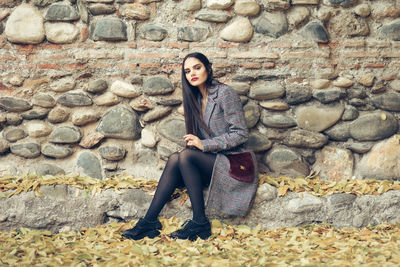 Portrait of beautiful model sitting against wall during autumn
